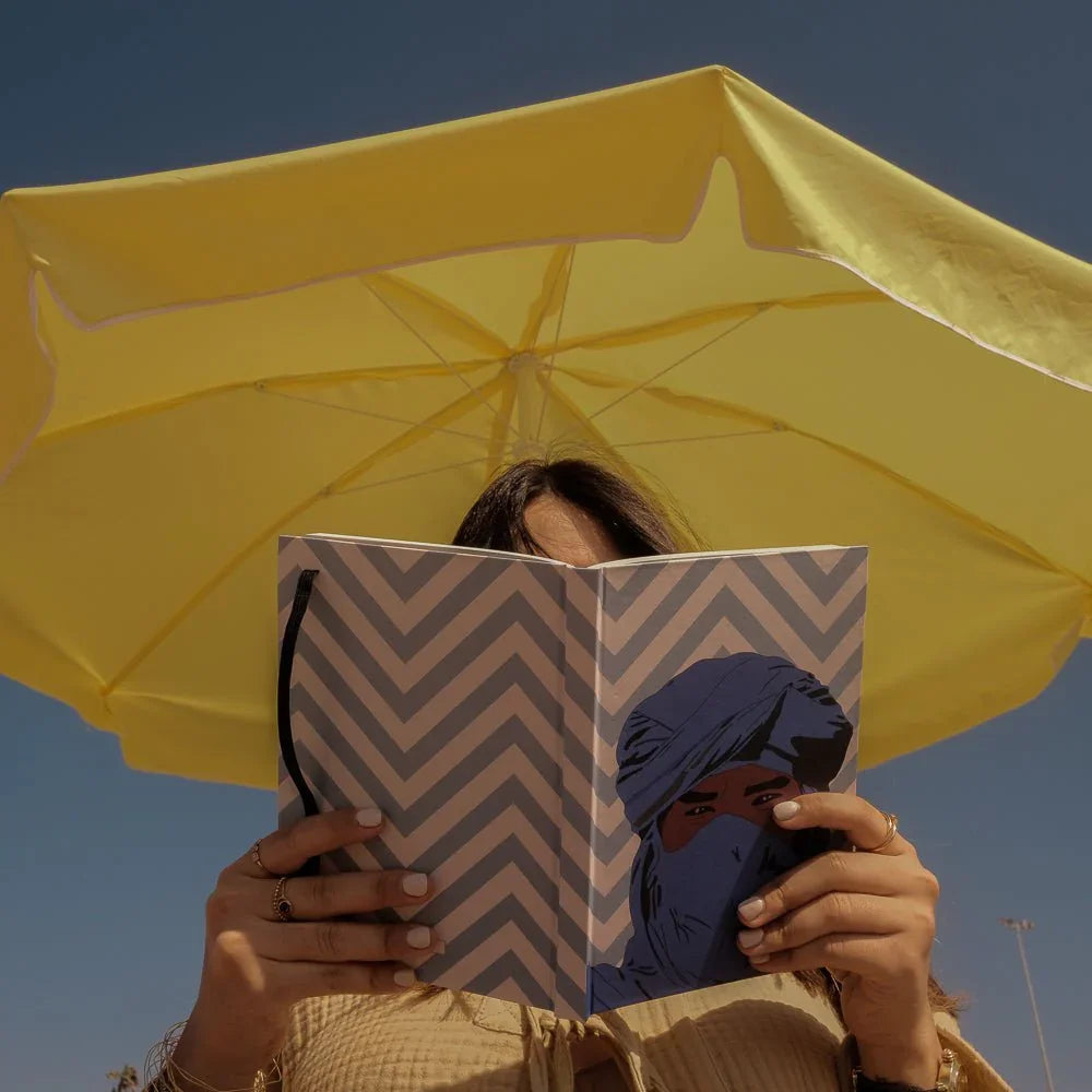 Woman reading ethnik Moroccan notebook with chevron cover under yellow umbrella