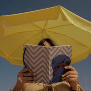 Woman reading ethnik Moroccan notebook with chevron cover under yellow umbrella