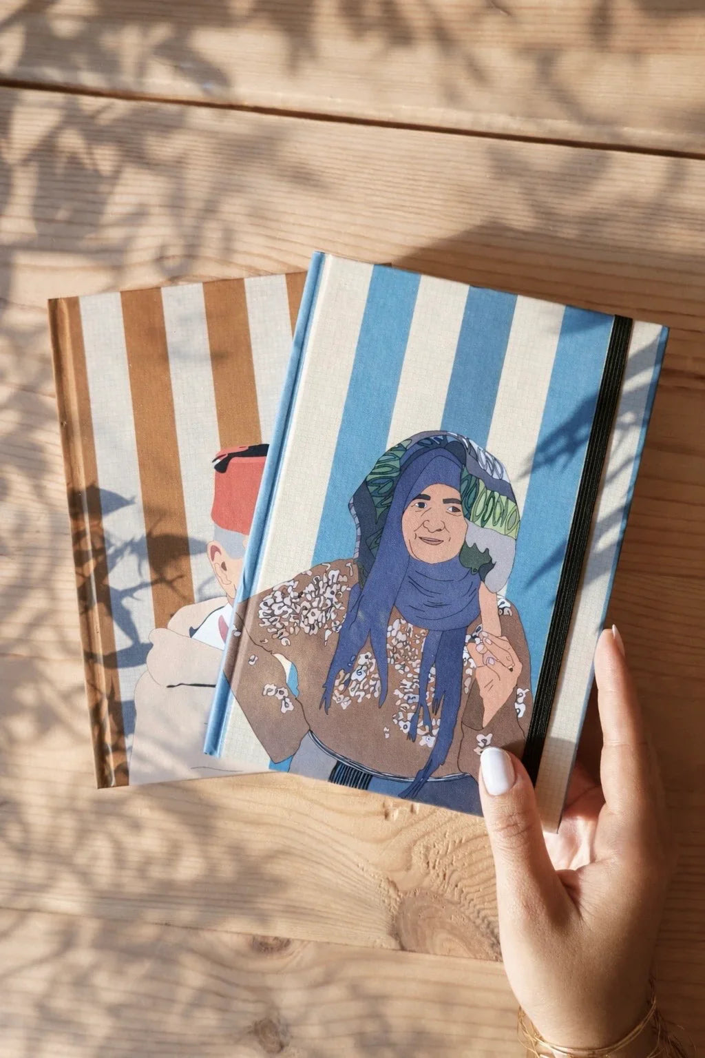 Hand holding ethnik Moroccan illustrated notebooks with striped covers on wood table