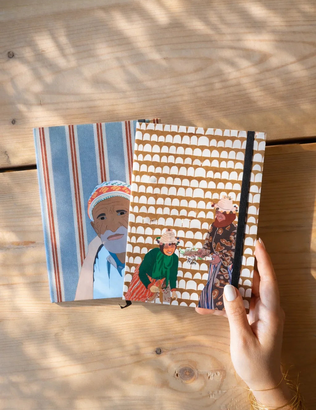Hand holding Moroccan illustrated ethnik notebooks on wooden table, original stationery design