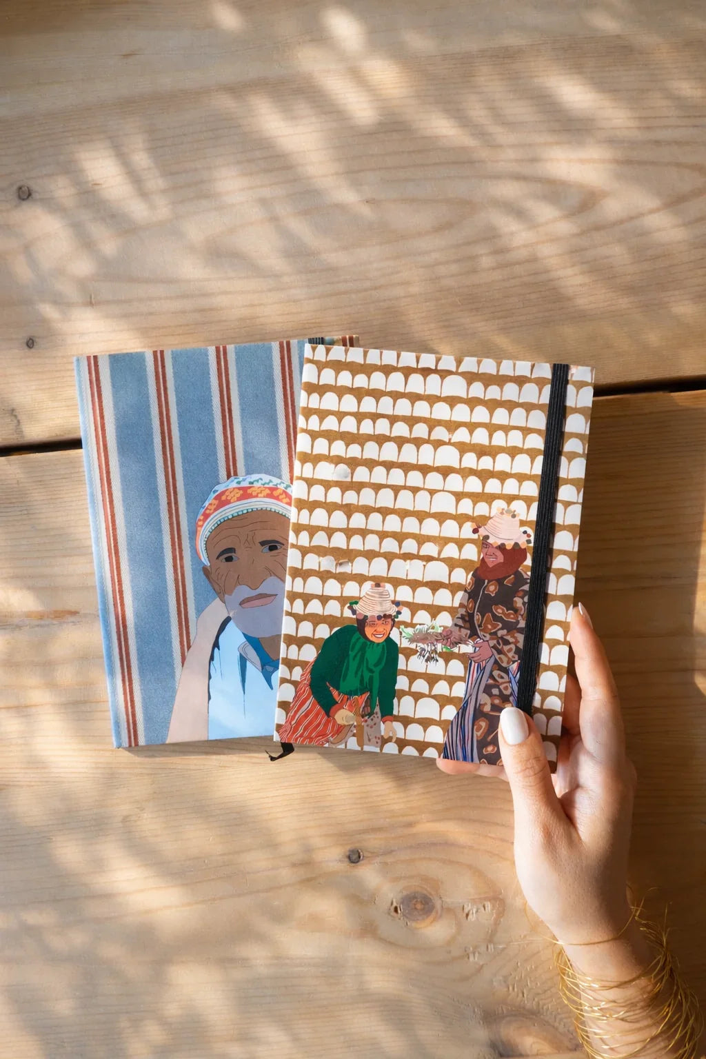 Hand holding Moroccan illustrated ethnik notebooks on wooden table, original stationery design