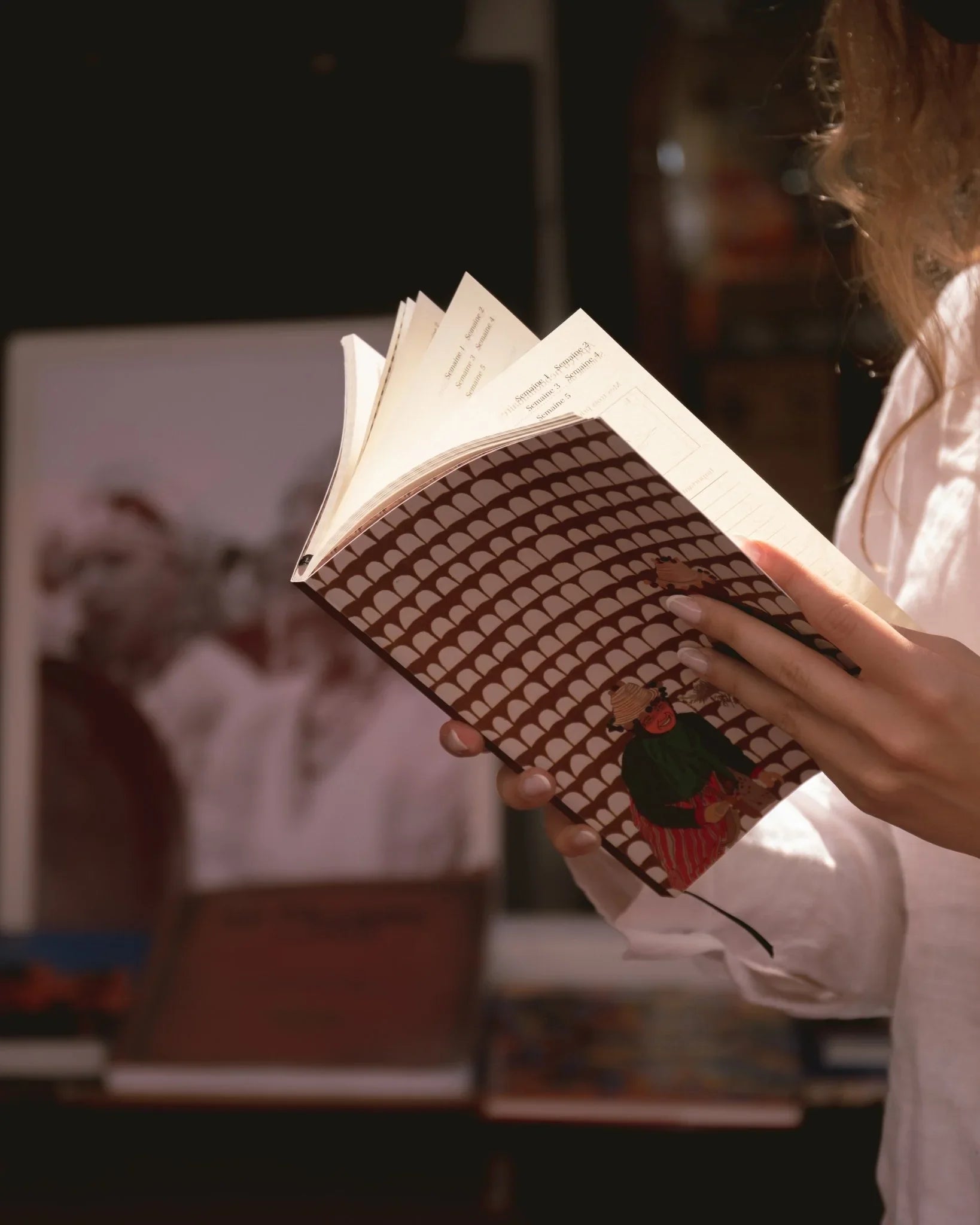 Person holding ethnik Morocco illustrated notebook, brown patterned cover, warm indoor light.