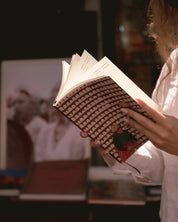 Person holding ethnik Morocco illustrated notebook, brown patterned cover, warm indoor light.