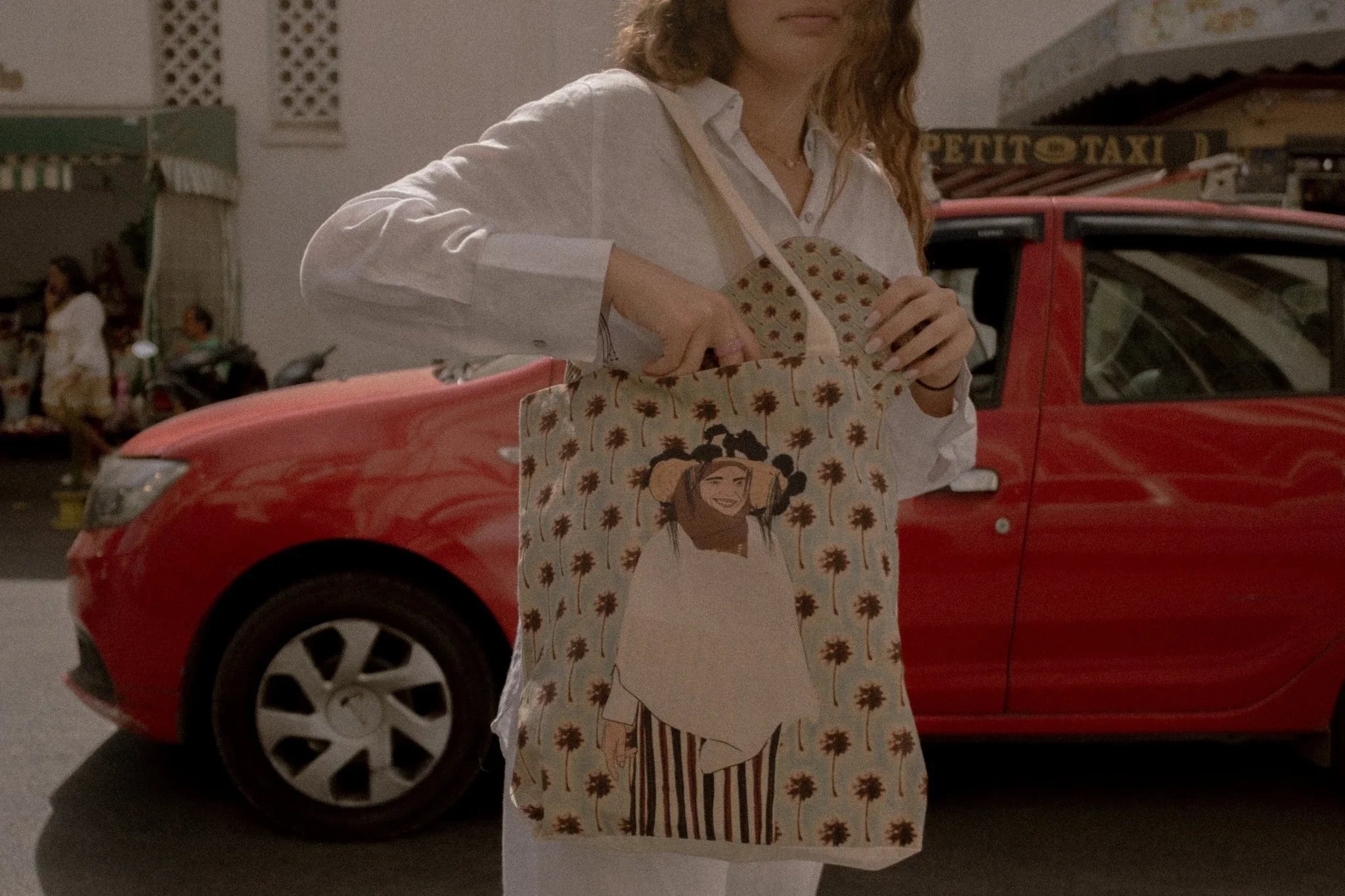 Woman holding ethnik tote bag with Moroccan illustration, standing by red car in city street