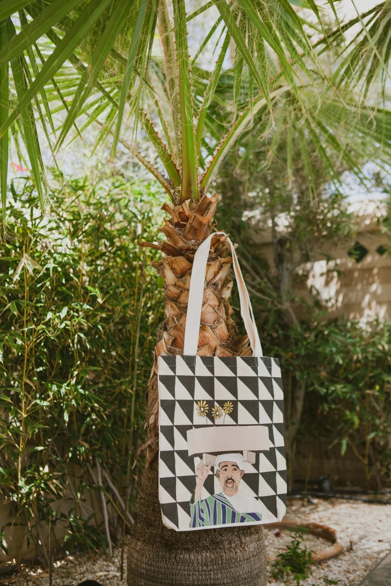 Ethnik Morocco tote bag with geometric black and white pattern and illustrated figure, hanging on palm tree