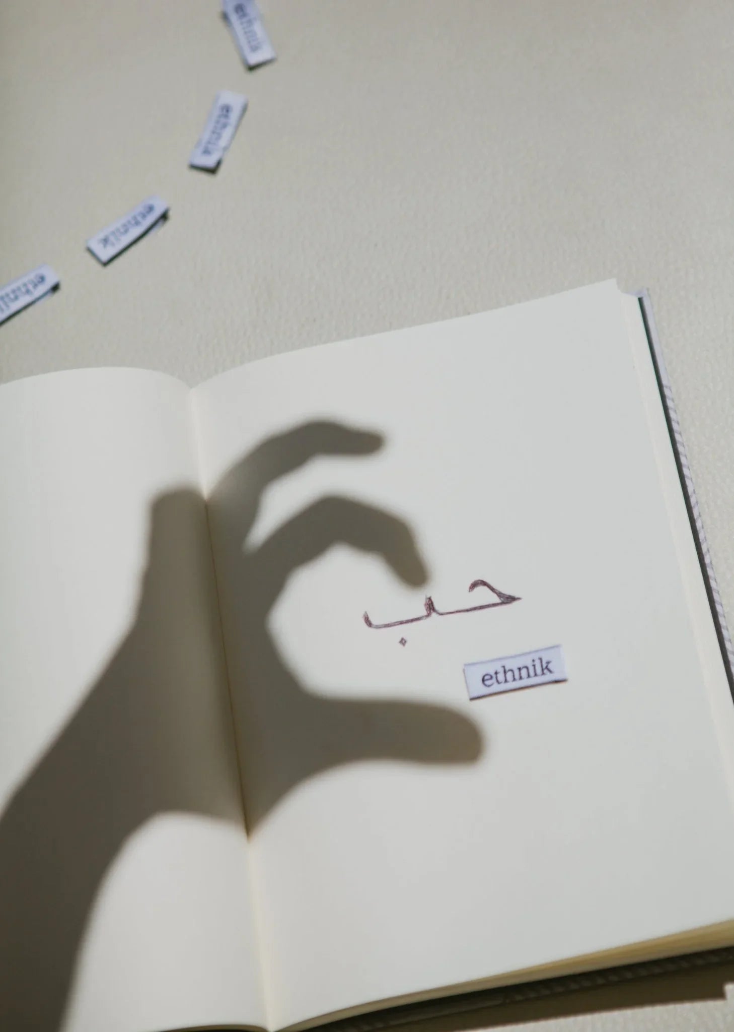Open notebook with Arabic calligraphy, ethnik label, and shadowed hand on blank page