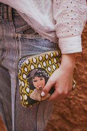 Hand holding ethnik Moroccan illustrated pouch against denim jeans and lace top