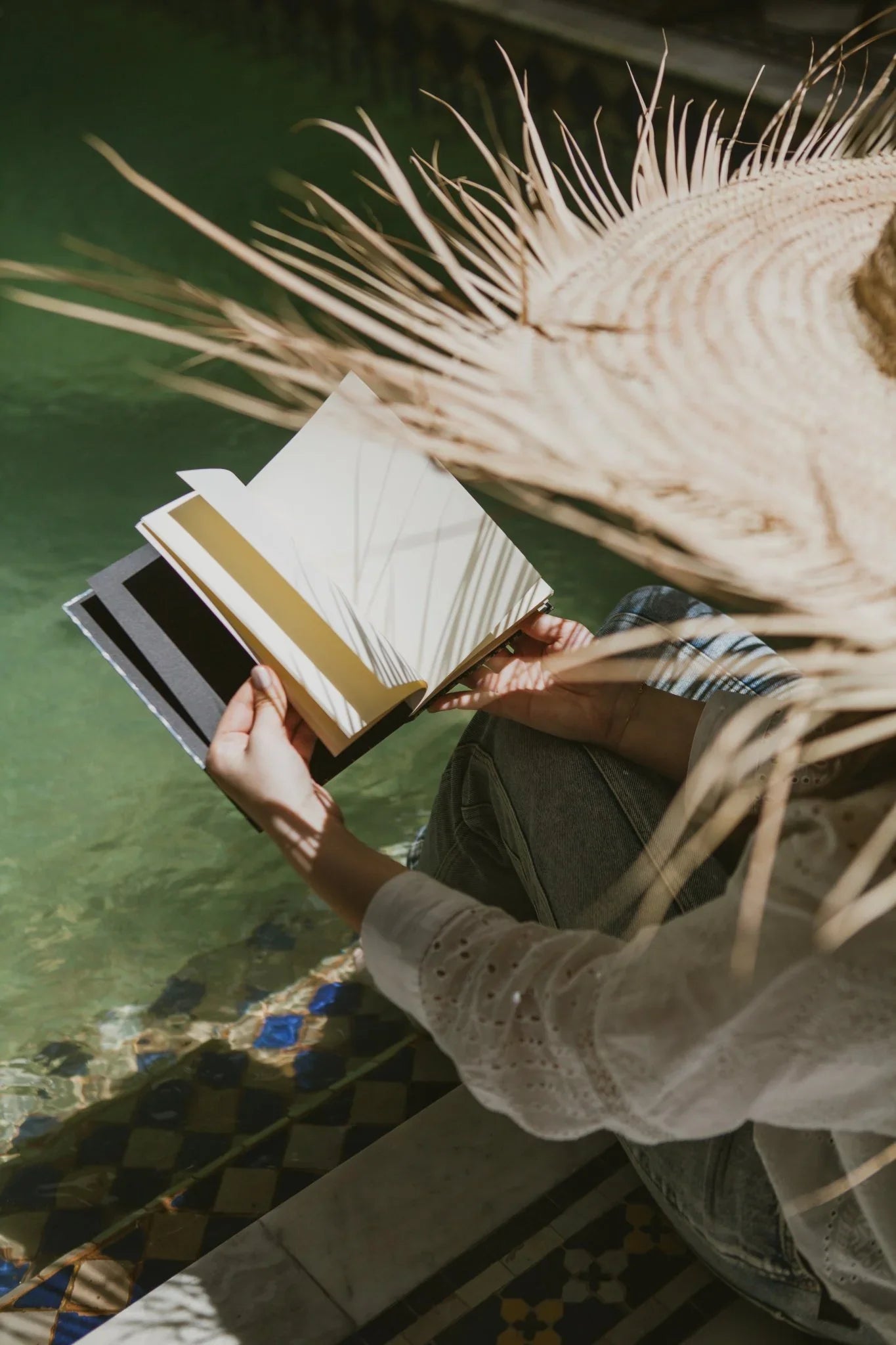 Person with straw hat holding ethnik stationery notebook by Moroccan pool