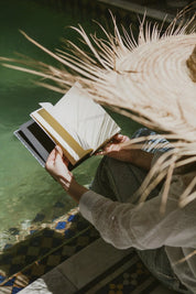 Person with straw hat holding ethnik stationery notebook by Moroccan pool