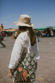 Woman wearing a beige hat and white top with an Ethnik illustrated tote bag in a Moroccan market