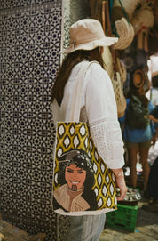 Woman wearing a hat and white blouse carrying a Moroccan illustrated tote bag by ethnik in a market