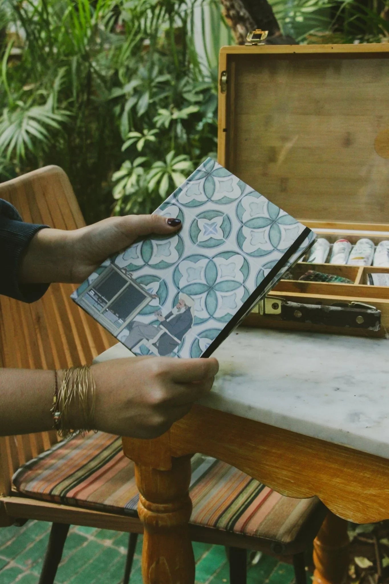 Person holding ethnik patterned Moroccan notebook near artist paint box outdoors