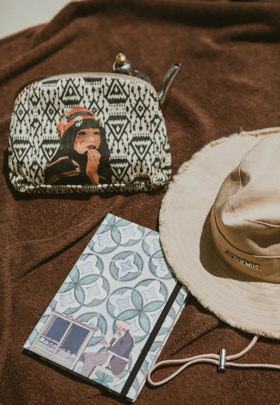 Moroccan illustrated pouch, patterned notebook, and beige hat on brown fabric from ethnik.