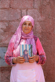Moroccan woman in pink hijab holding ethnik illustrated notebook, brick wall background