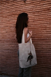 Woman with long hair holding ethnik tote bag featuring original Moroccan illustration, brick wall backdrop