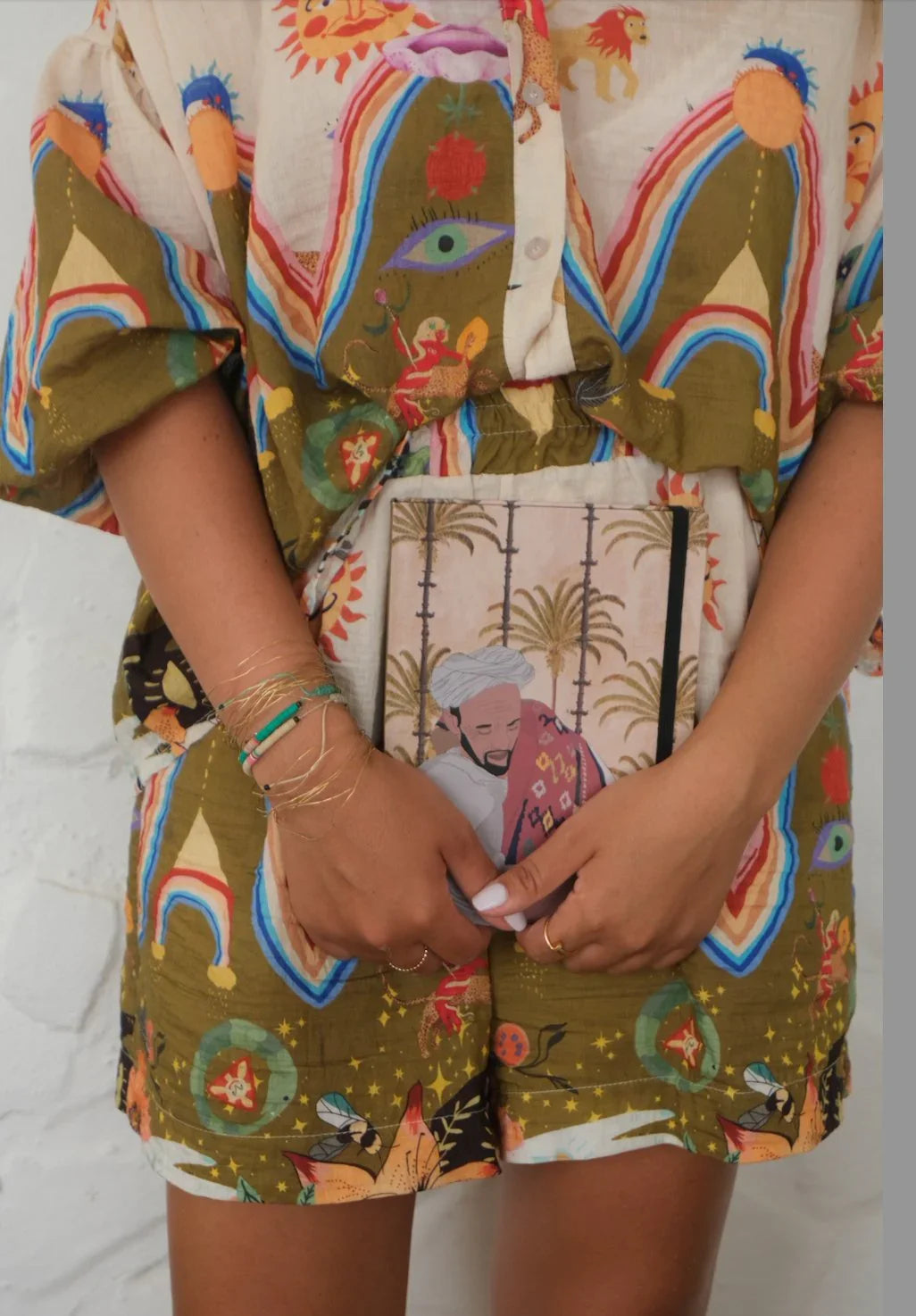 Colorful Moroccan-inspired shirt and shorts set, holding an ethnik illustrated stationery notebook.