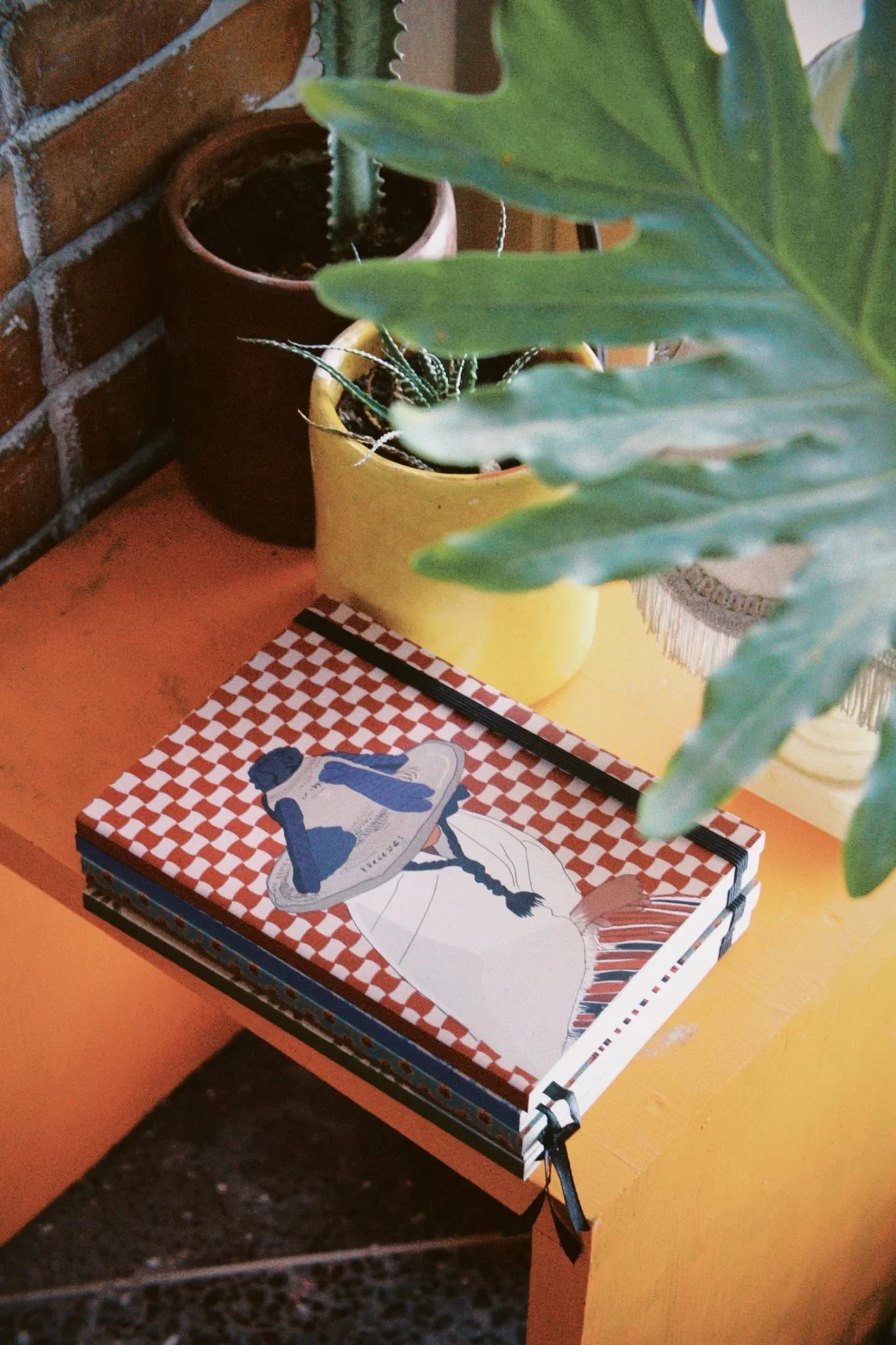 ethnik Moroccan illustrated notebook with checkered cover on orange table, potted plants nearby