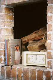 Ethnik Moroccan illustrated stationery notebooks and vintage clock on a brick fireplace with wood.