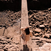 Woman in beige coat on rocky path holding patterned ethnik tote bag, natural sunlight