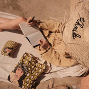 Woman drawing in notebook, wearing straw hat with 'ethnik' text, with Moroccan illustrated pouches.