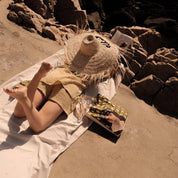 Woman relaxing on beach with large straw hat, ethnik tote bag, and original Morocco illustration.